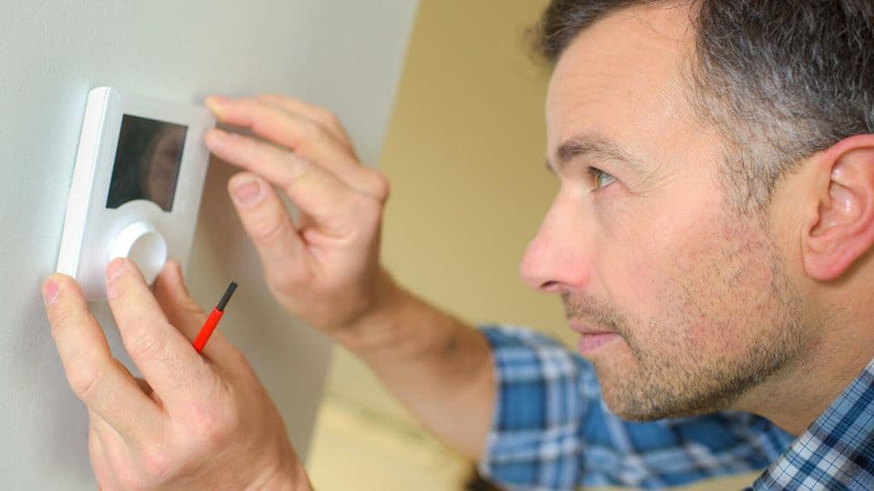 Elektriker bringt ein Thermostat in einem Zimmer an.