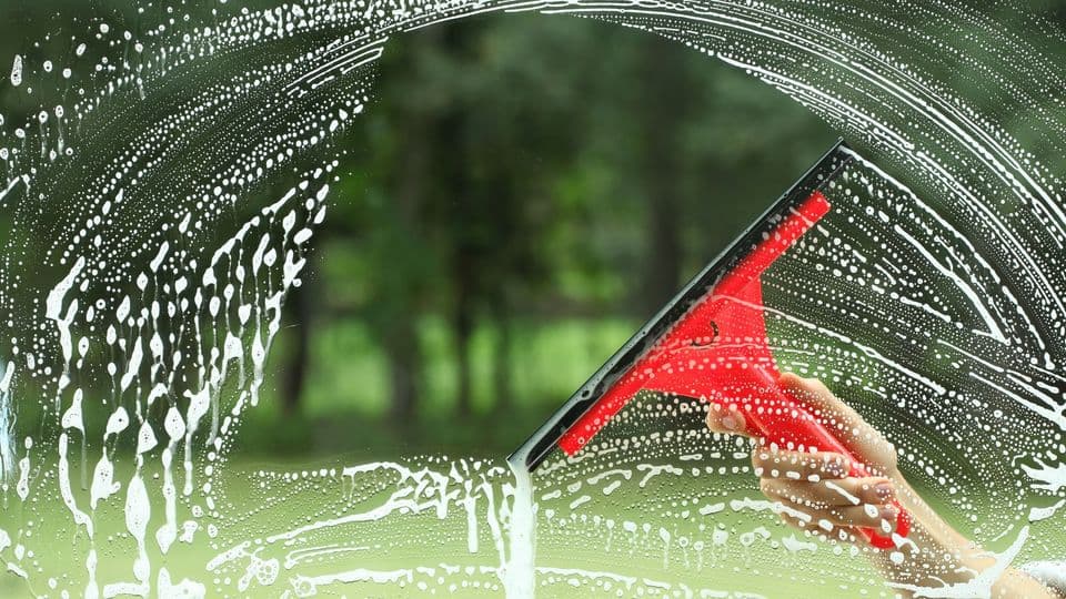 Eine Person putzt ein Fenster, sodass die Sicht nach draußen wieder frei ist