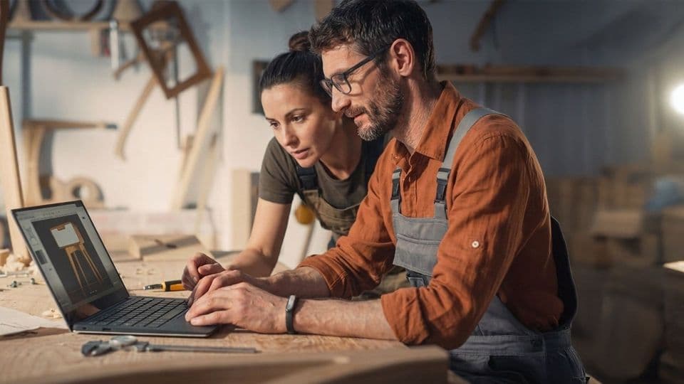 Eine Handwerkerin und ein Handwerker arbeiten gemeinsam an einem Computer und schauen sich etwas an.