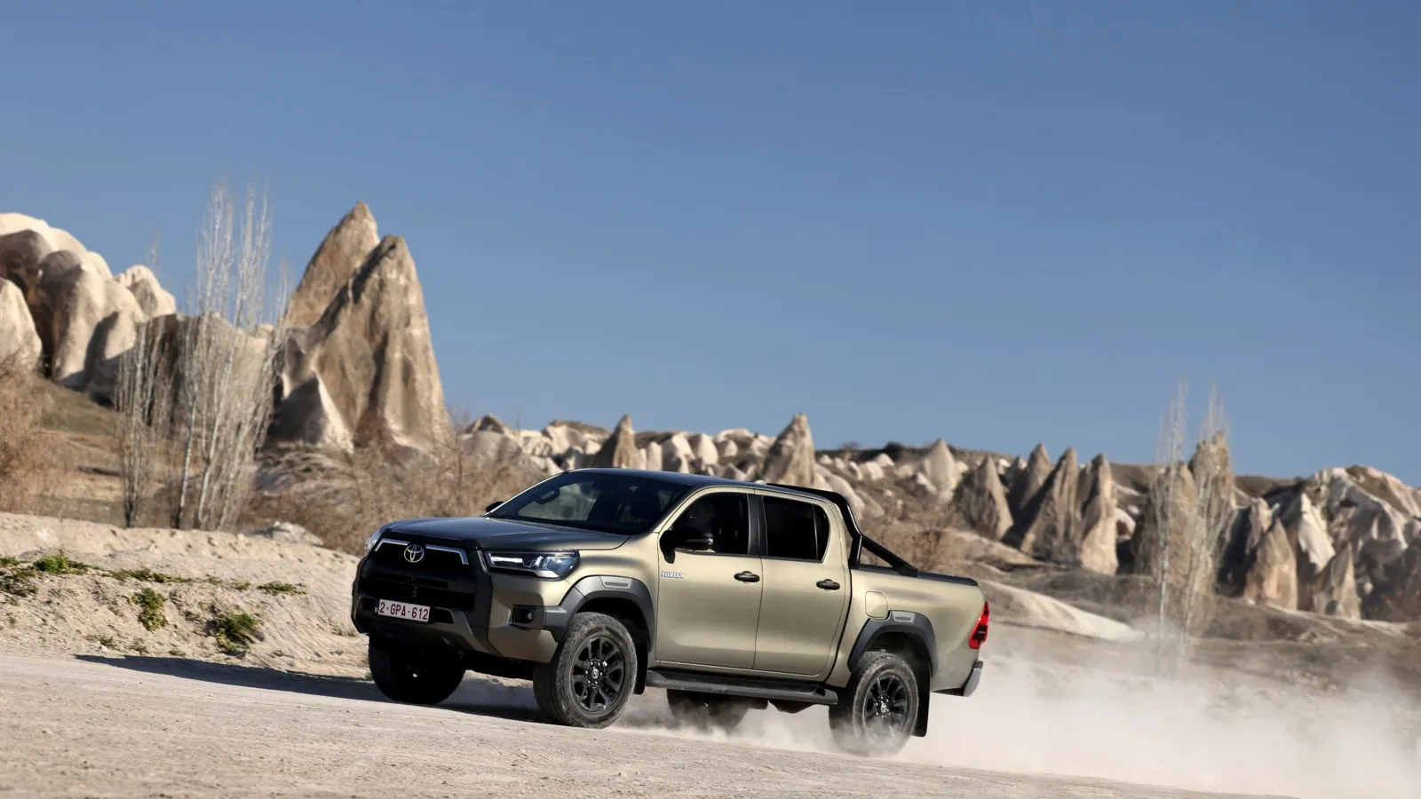 Der neue Hilux Hybrid in gold/bronze fährt auf einer wüstenartigen Landschaft.
