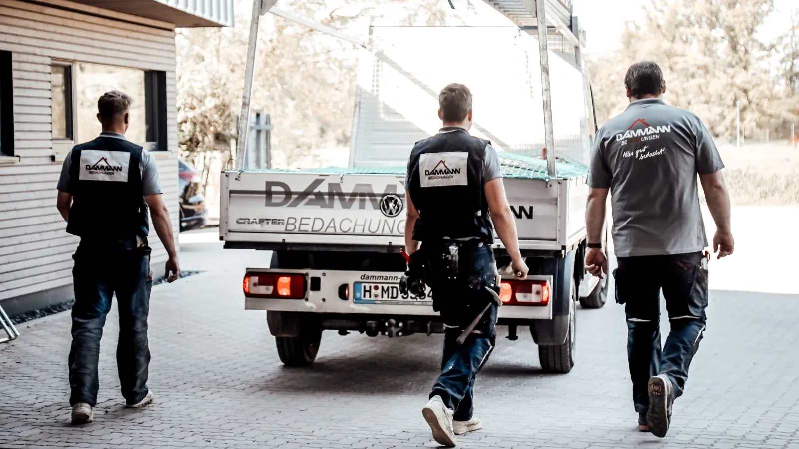 Drei Handwerker gehen auf einen Pick-Up von Dammann zu. Sie sind von hinten zu sehen in ihrer Arbeitsbekleidung.