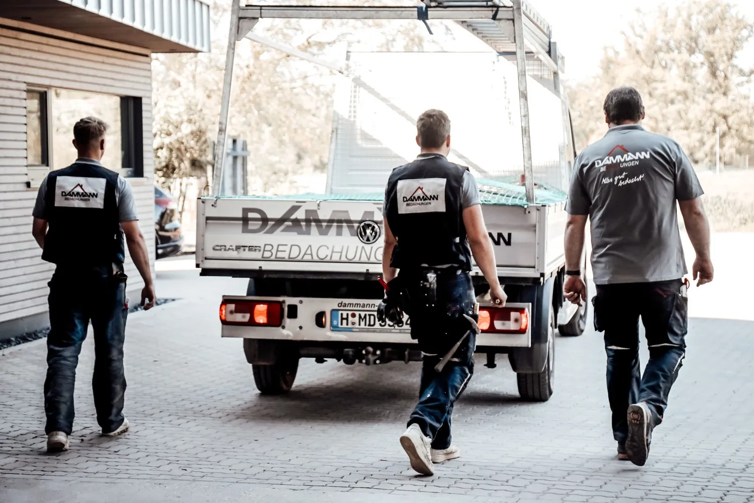 Drei Handwerker gehen auf einen Pick-Up von Dammann zu. Sie sind von hinten zu sehen in ihrer Arbeitsbekleidung.