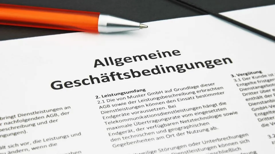 Allgemeine Geschäftsbedingungen liegen ausgedruckt mit einem  orangefarbenen Kugelschreiber auf einer schwarzen Mappe