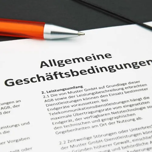 Allgemeine Geschäftsbedingungen liegen ausgedruckt mit einem  orangefarbenen Kugelschreiber auf einer schwarzen Mappe