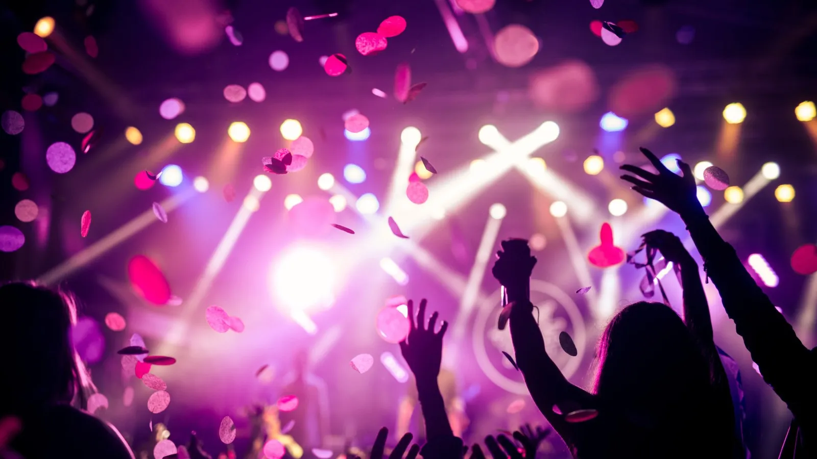 Partyatmosphäre mit weiß und lila Lichtern und tanzenden Menschen.