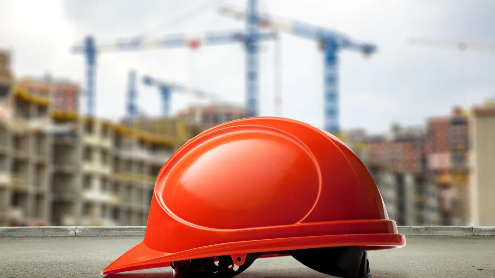Ein roter Schutzhelm liegt auf dem Boden, im Hintergrund ist eine Baustelle.