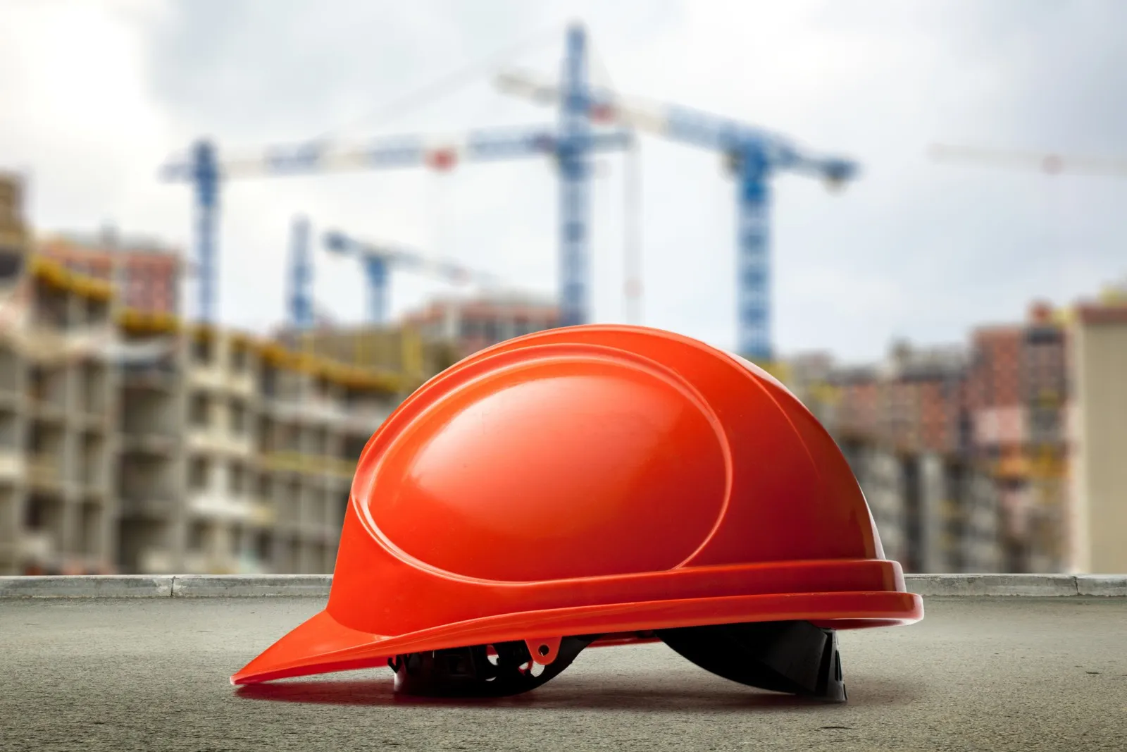 Ein roter Schutzhelm liegt auf dem Boden, im Hintergrund ist eine Baustelle.