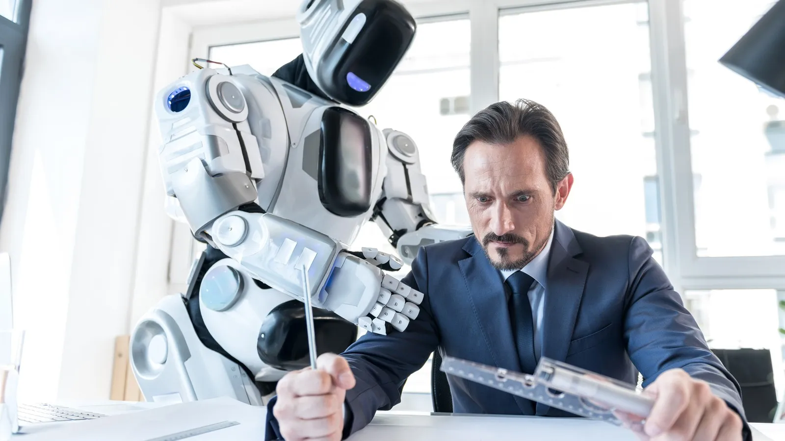 Mann am Schreibtisch ist ärgerlich auf einen Roboters, der hinter ihm steht