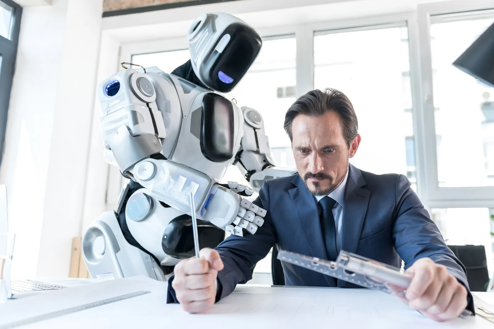 Mann am Schreibtisch ist ärgerlich auf einen Roboters, der hinter ihm steht