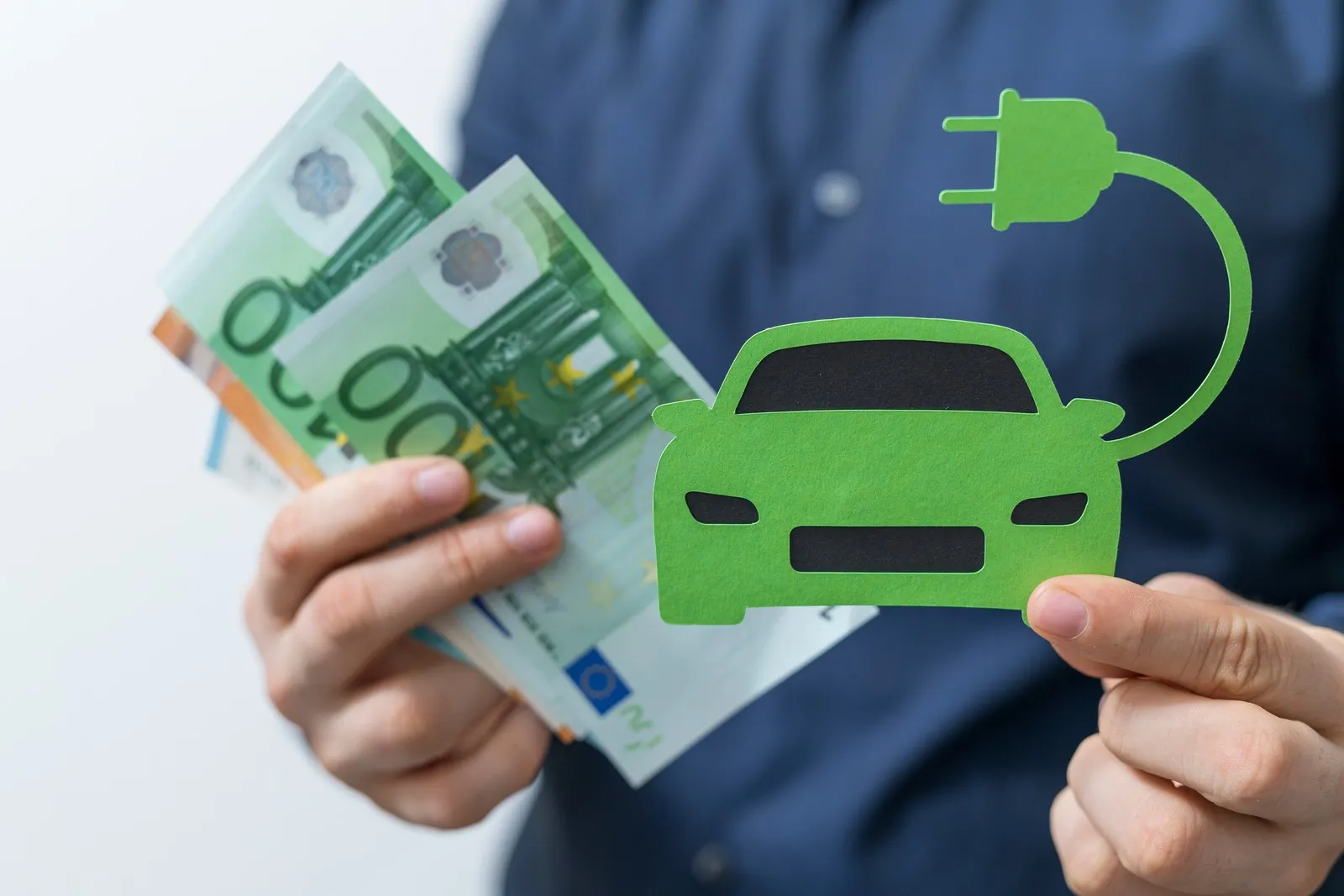 Mann hält ein E-Auto in der Hand und in der anderen Hand hat er mehrere Geldscheine