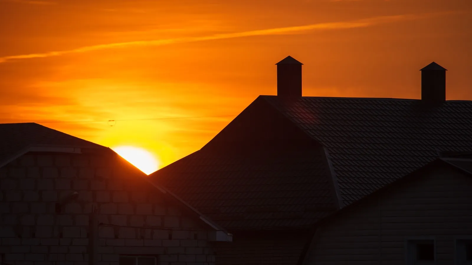 Silhouette eines Hausdachs vor einem farbenreichen Abendhimmel bei Sonnenuntergang.