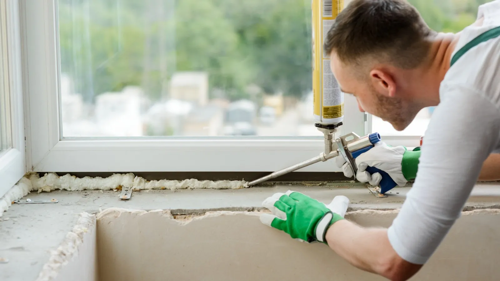 Ein Handwerker dichtet ein Fenster mit Fensterschaum ab.