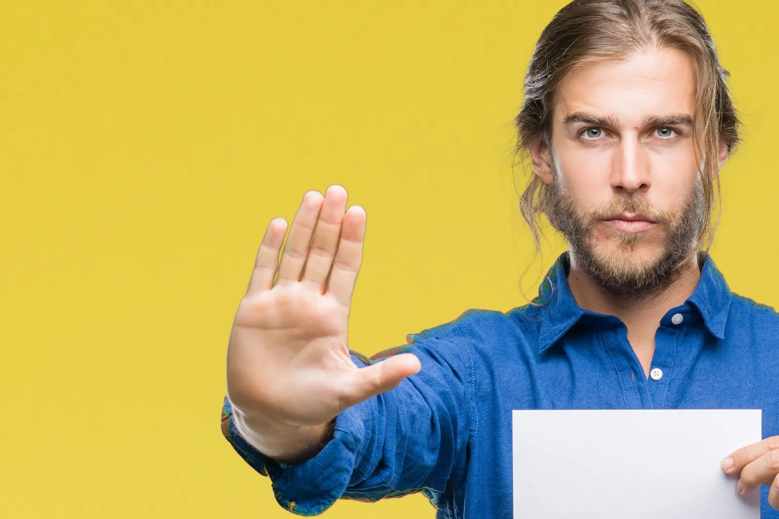  Mann steht vor einem gelben Hintergrund und hat ein Blatt papier in der Hand – mit der anderen Hand gestikuliert er "Stop"