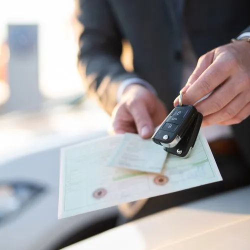 Autohändler steht mit Autoschlüsseln und Zulassungspapieren vor Neuwagen
