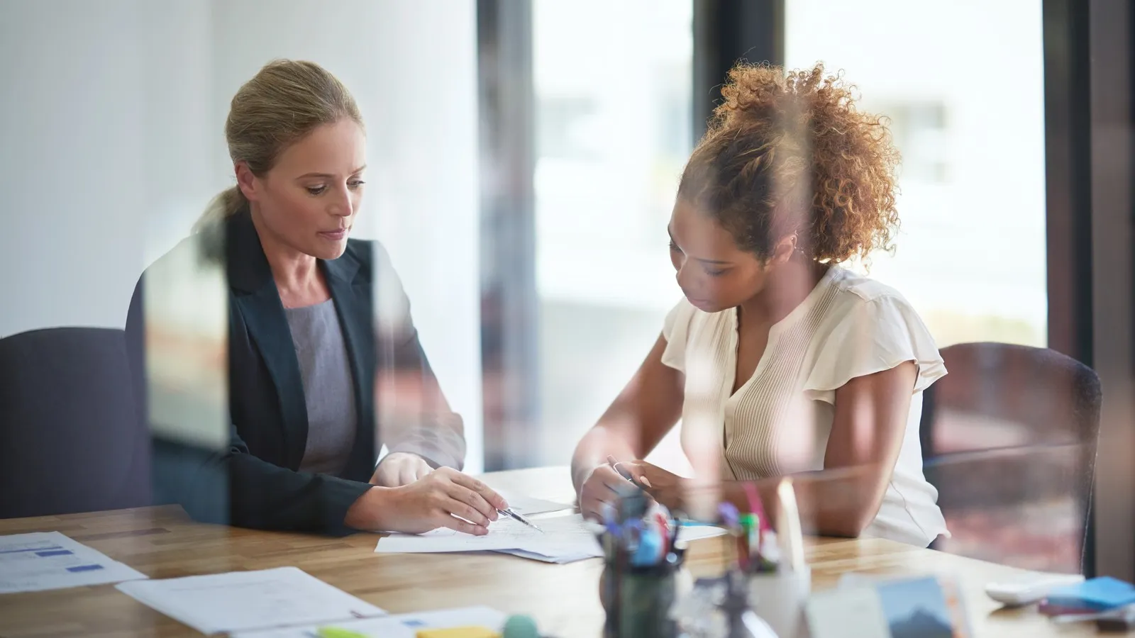 Zwei Frauen sitzen im Büro über ein Schriftstück gebeugt.