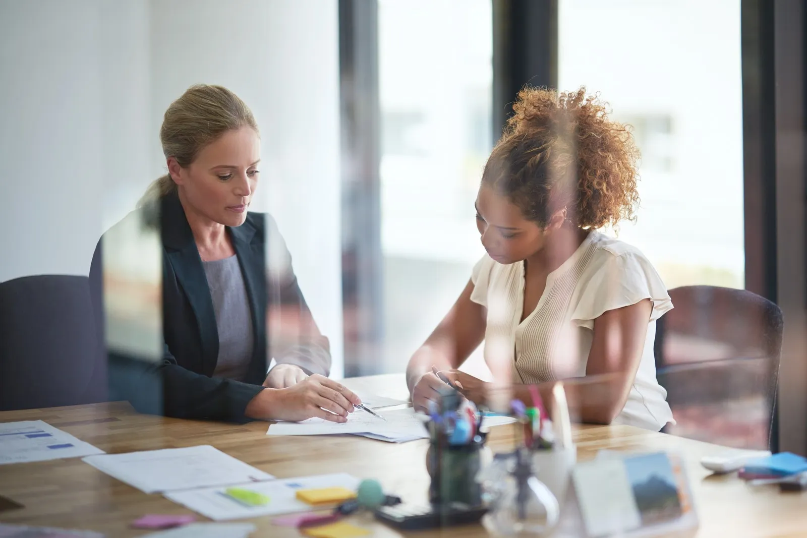 Zwei Frauen sitzen im Büro über ein Schriftstück gebeugt.