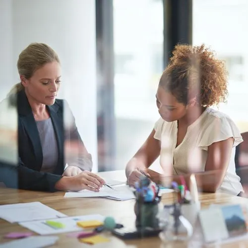 Zwei Frauen sitzen im Büro über ein Schriftstück gebeugt.