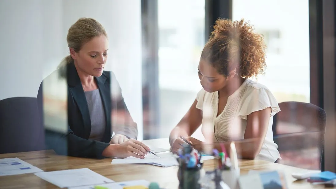 Zwei Frauen sitzen im Büro über ein Schriftstück gebeugt.