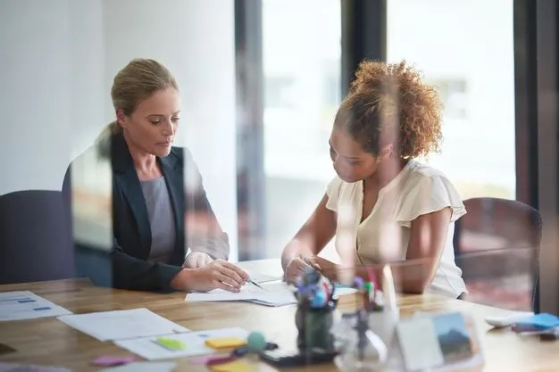 Zwei Frauen sitzen im Büro über ein Schriftstück gebeugt.