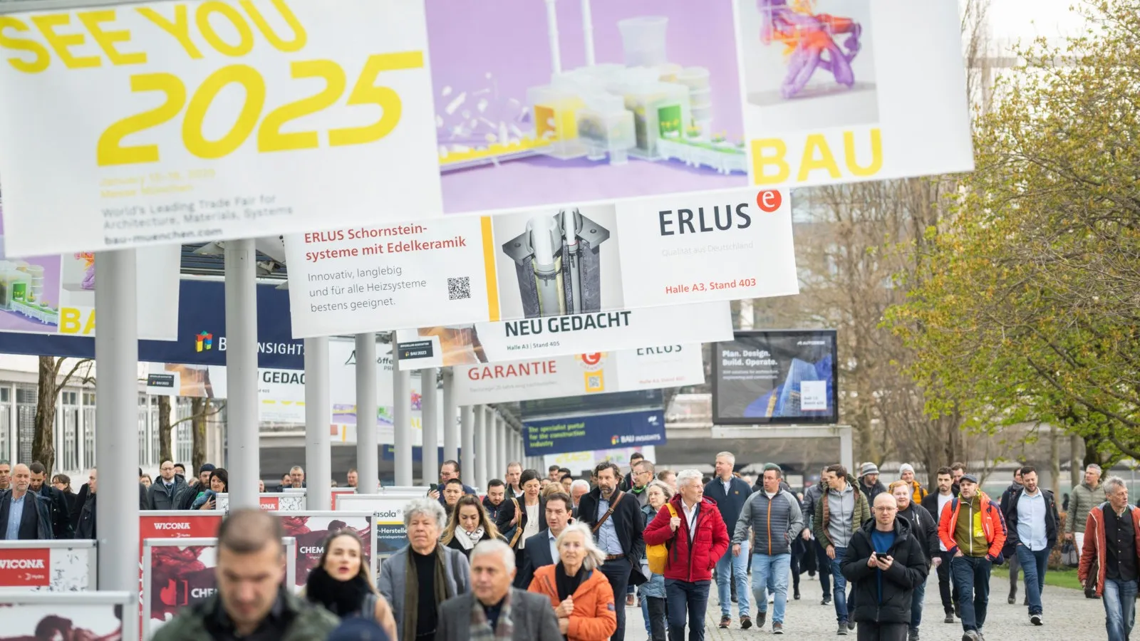 Foto von vielen Menschen draußen, über ihnen hängen mehrere Banner für die Messe Bau 2025.