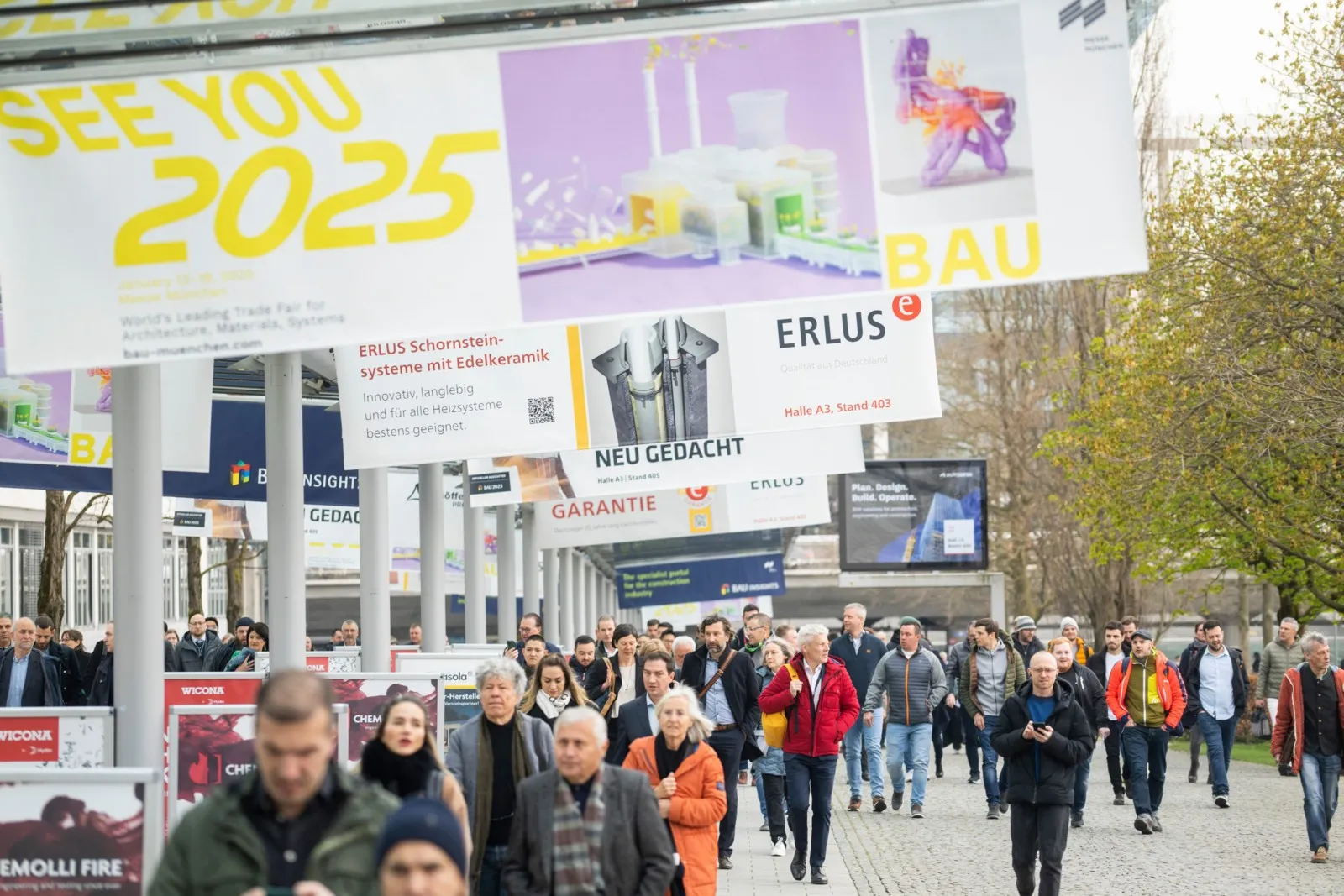 Foto von vielen Menschen draußen, über ihnen hängen mehrere Banner für die Messe Bau 2025.