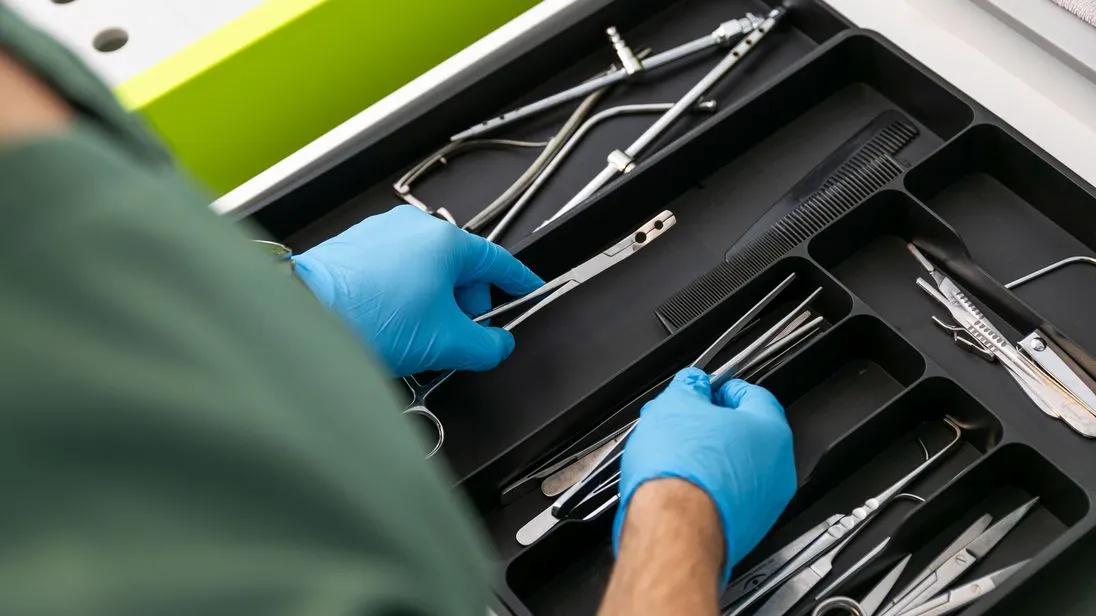 In Einmalhandschuhe gekleidete Hände wählen medizinisches Besteck aus einem Besteckkasten aus.