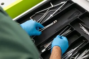In Einmalhandschuhe gekleidete Hände wählen medizinisches Besteck aus einem Besteckkasten aus.