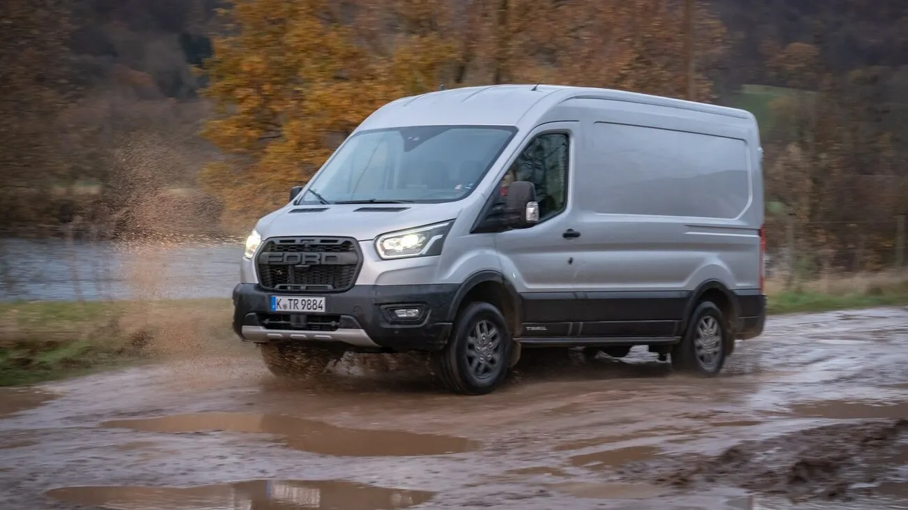 Der Ford Transit Trail 4x4 fährt an einem See vorbei auf nassem erdigen Boden.