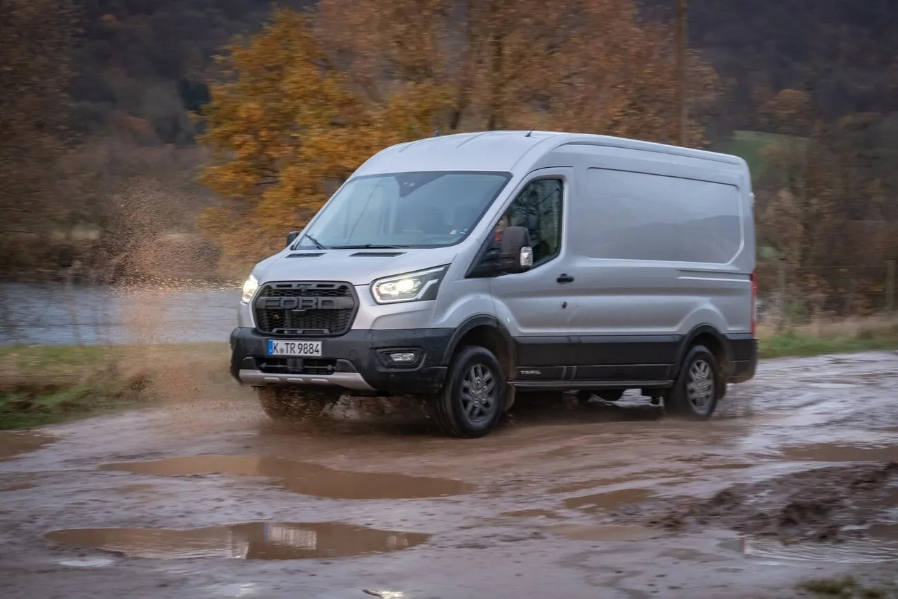 Der Ford Transit Trail 4x4 fährt an einem See vorbei auf nassem erdigen Boden.