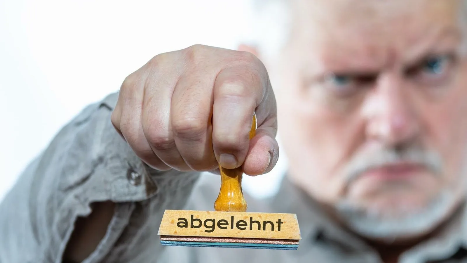 Ein Mann schaut grimmig und hält einen Stempel mit der Aufschrift "Abgelehnt" in den Fokus.