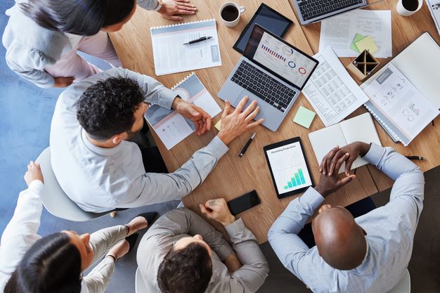 Businessmeeting: Junge Menschen sitzen an einem Tisch und planen an einem Laptop.