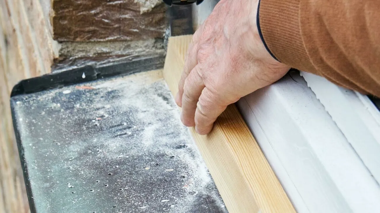 Ein Handwerker hält einen Holzschnitte an eine Fensterbank.