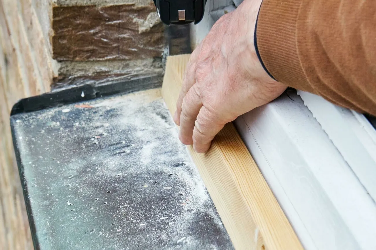 Ein Handwerker hält einen Holzschnitte an eine Fensterbank.