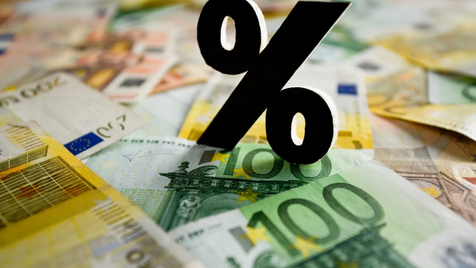 Mehrere Euro-Geldscheine liegen auf einer Oberfläche verteilt. Darauf steht ein schwarzes Prozentzeichen.
