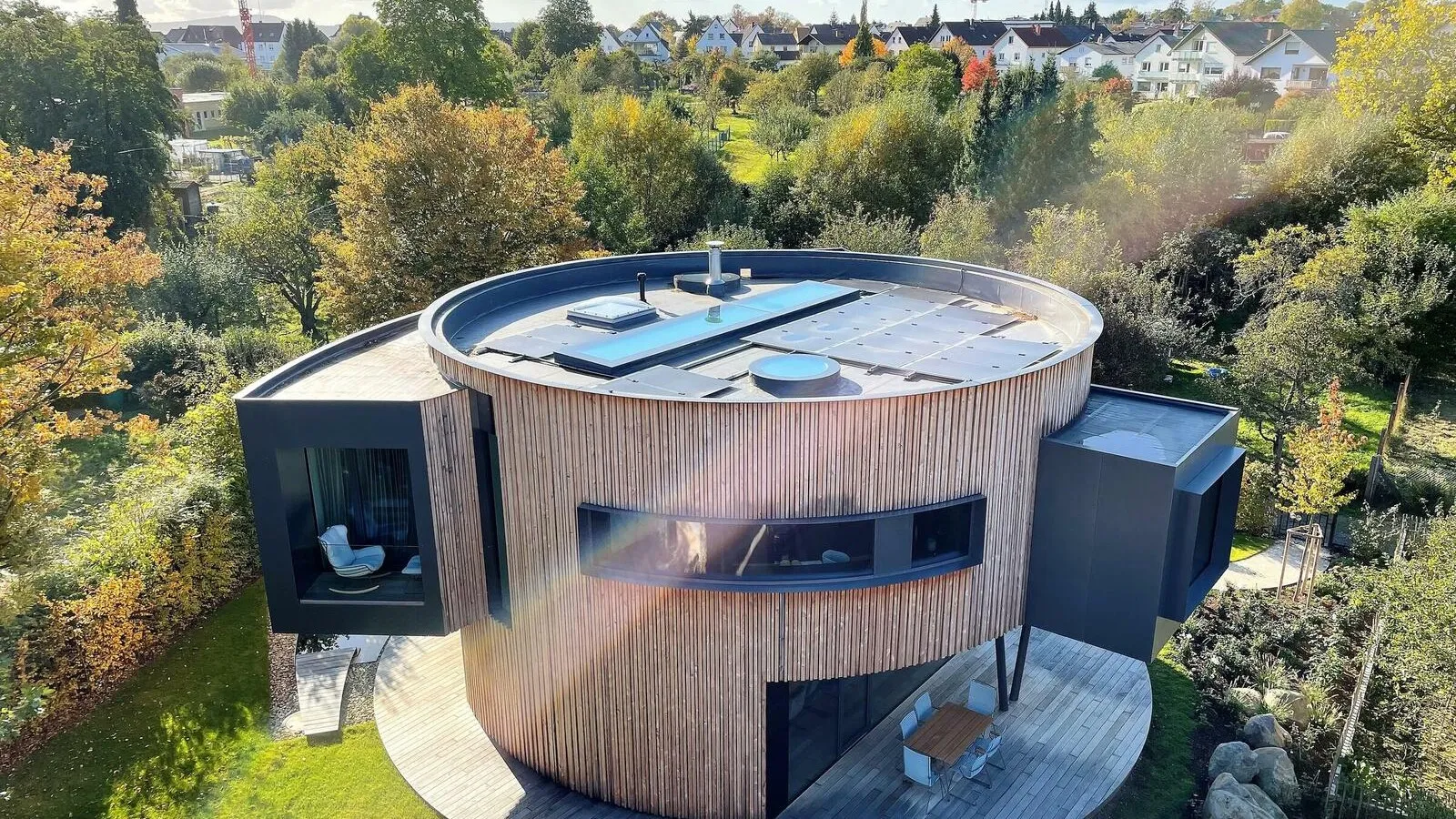 Ein Drehhaus in Holzoptik in einer grünen Umgebung mit einer Solaranlage auf dem Dach.