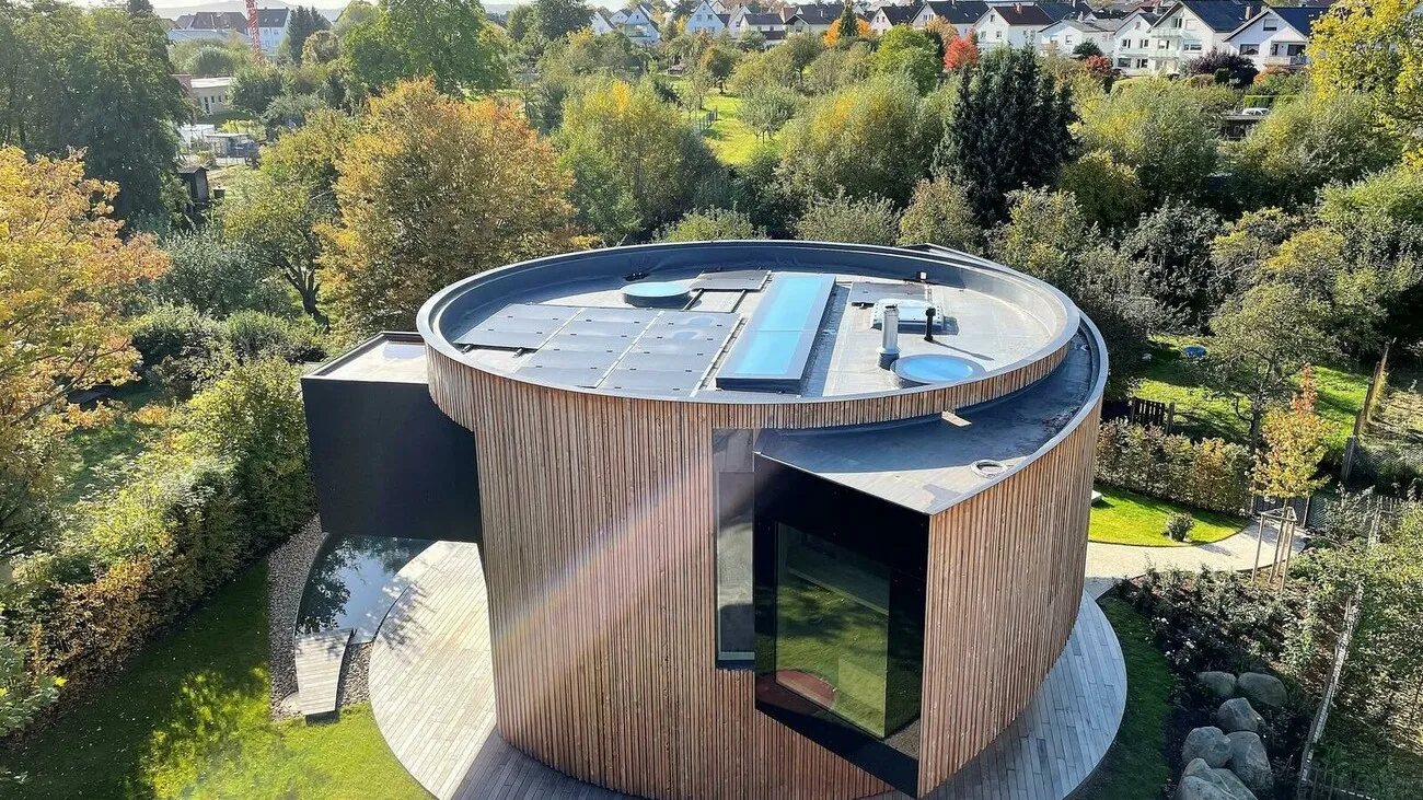 Ein Drehhaus mit Holzoptik und schwarzen großen Fenstern aus der Vogelperspektive, auf dem Dach befindet sich eine Solaranlage.