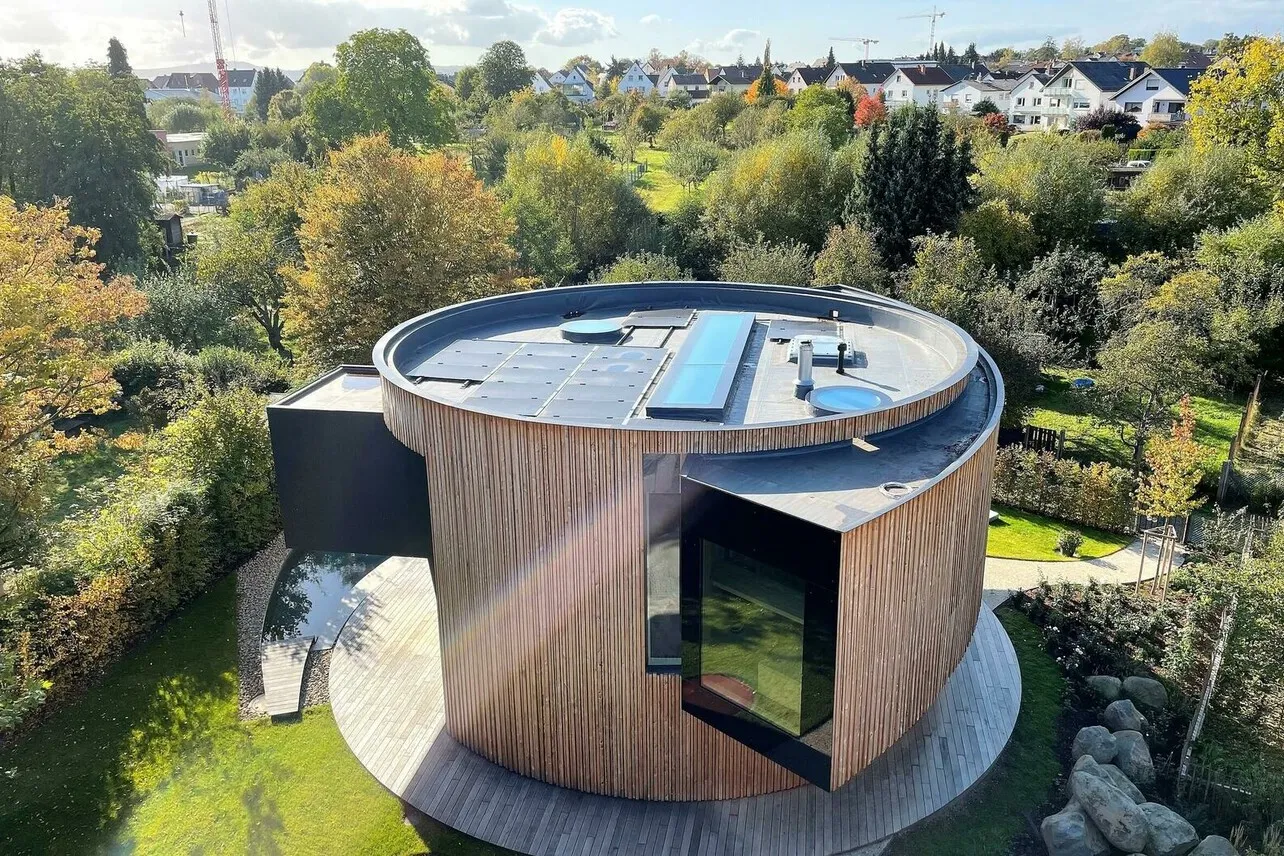 Ein Drehhaus mit Holzoptik und schwarzen großen Fenstern aus der Vogelperspektive, auf dem Dach befindet sich eine Solaranlage.