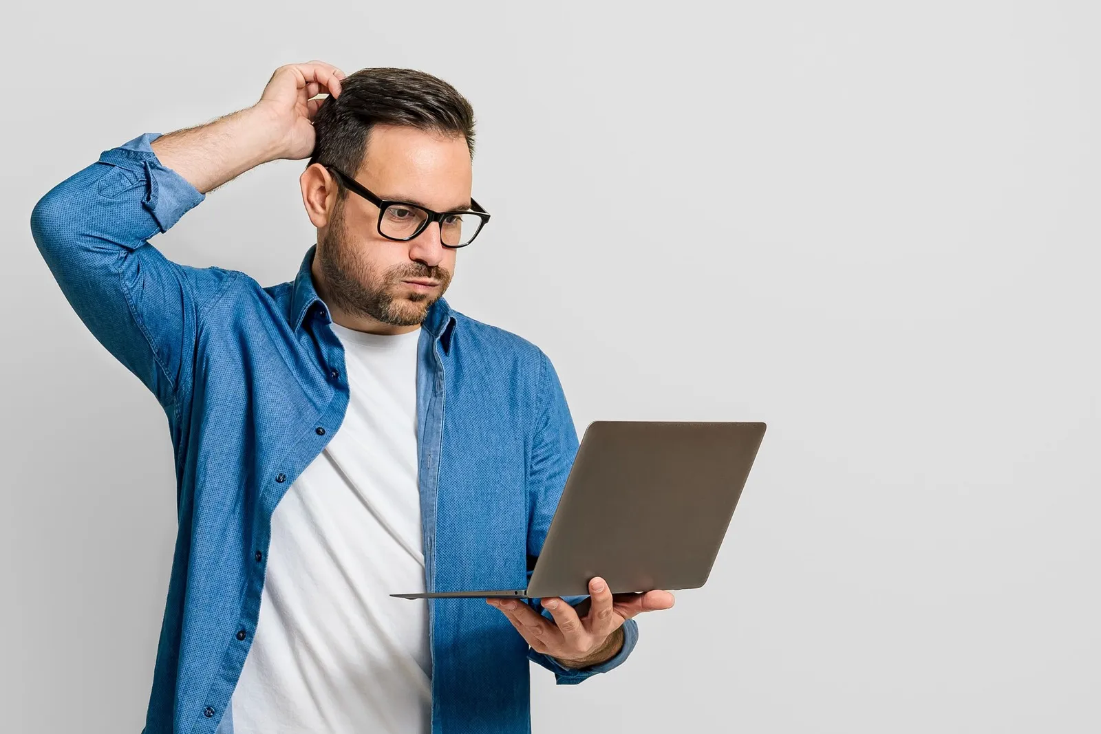 Mann schaut verzweifelt auf sein Laptop, das er in der Hand hält und kratzt sich am Kopf.