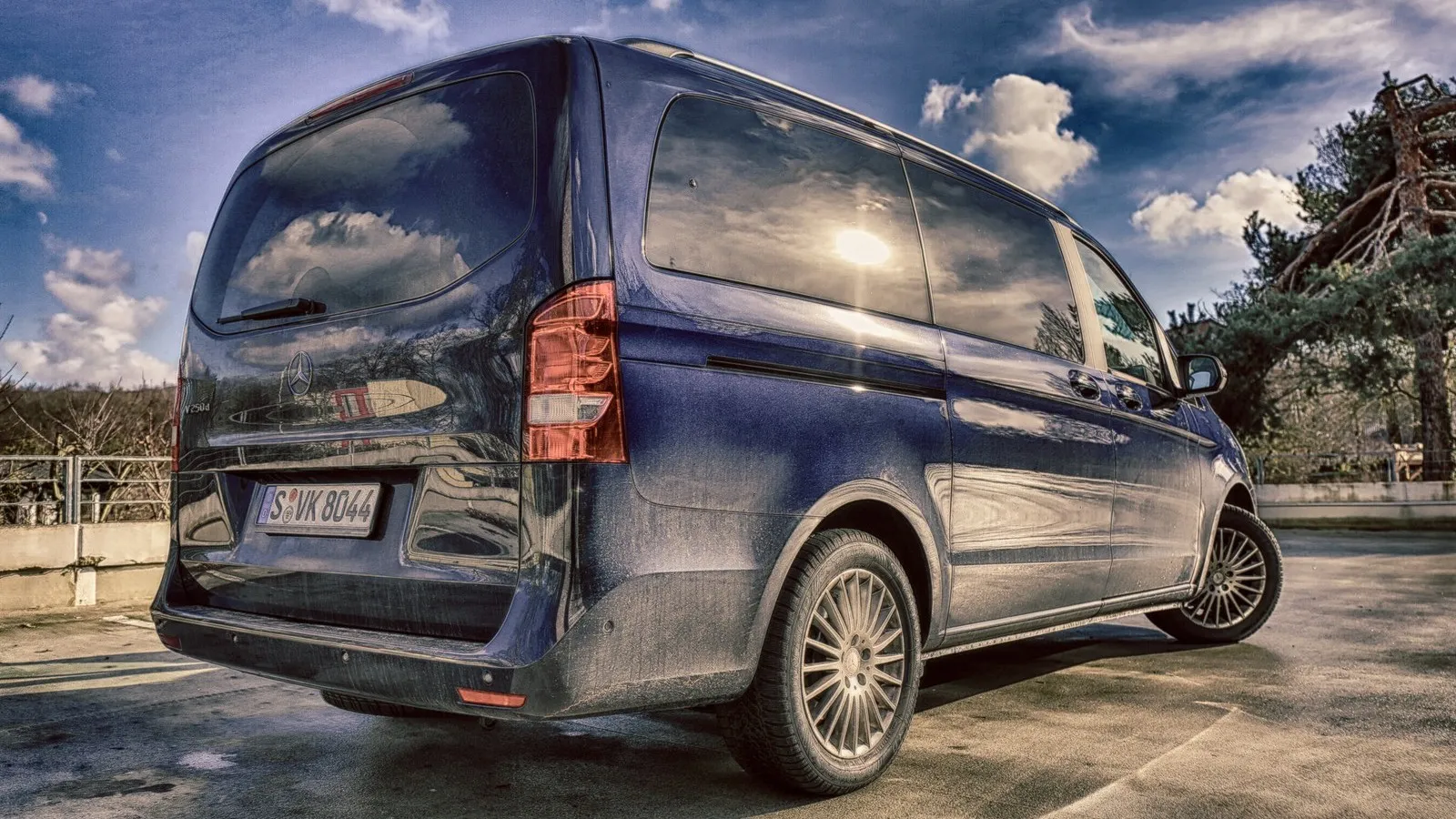 Ein verdreckter Mercedes Benz V-Klasse in dunkelblau seitlich von hinten.