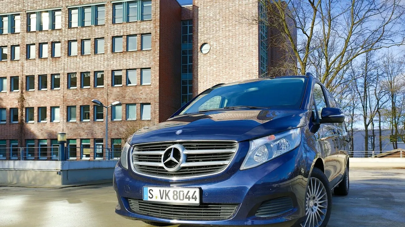 Die Mercedes V Klasse in dunkelblau von vorne. Im Hintergrund ist ein Wohngebäude zu sehen.