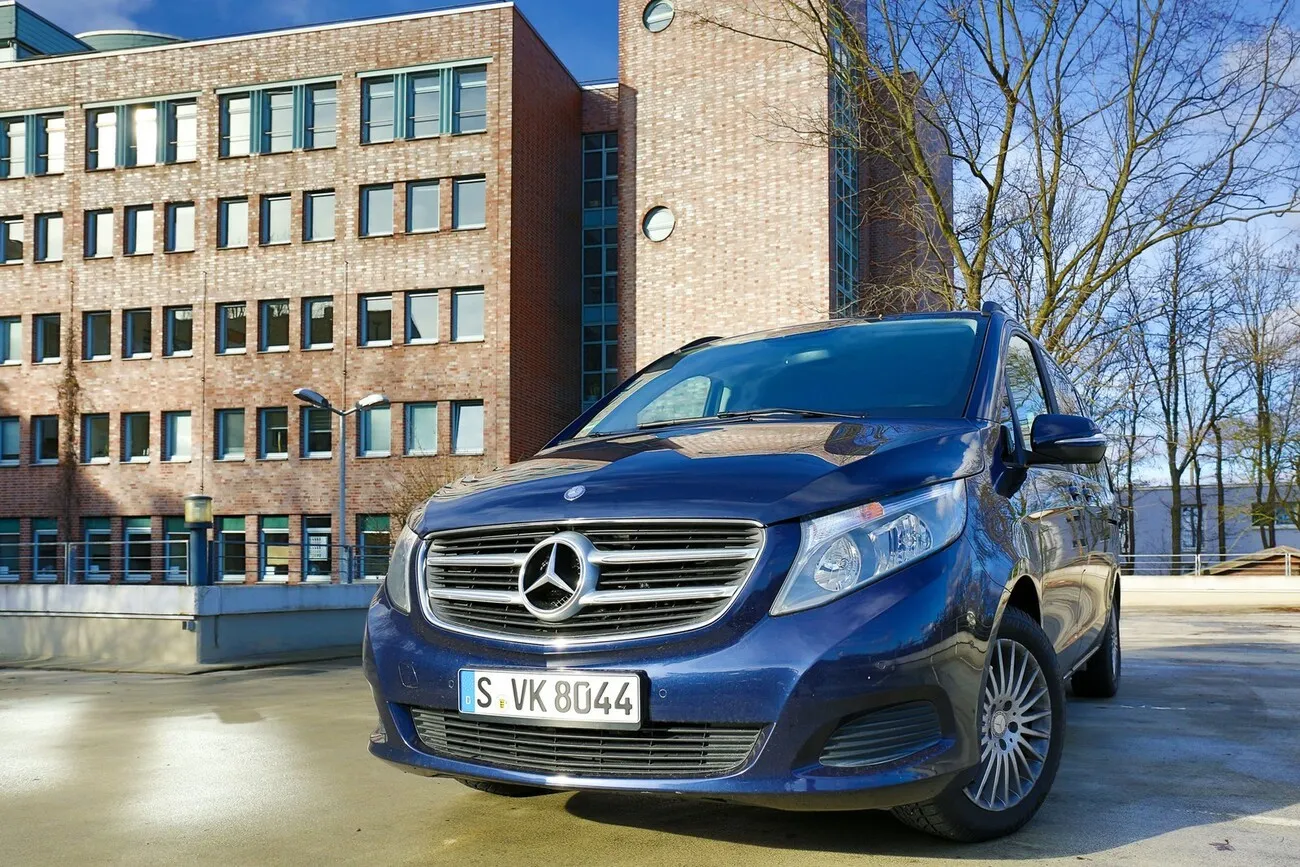 Die Mercedes V Klasse in dunkelblau von vorne. Im Hintergrund ist ein Wohngebäude zu sehen.