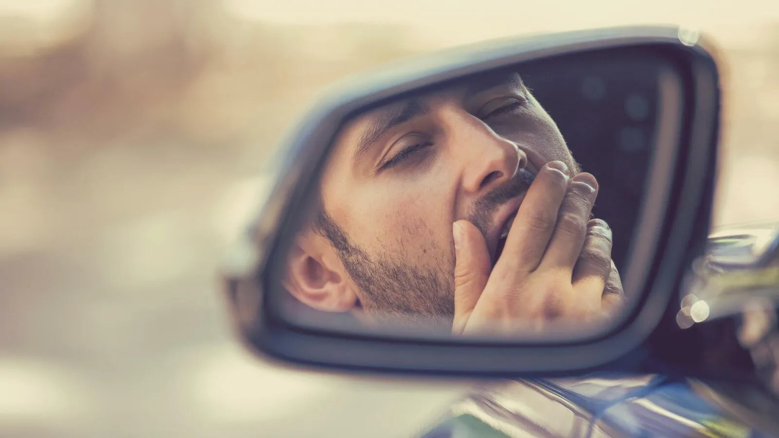 Das Spiegelbild eines Mannes im Seitenspiegel eines Autos.