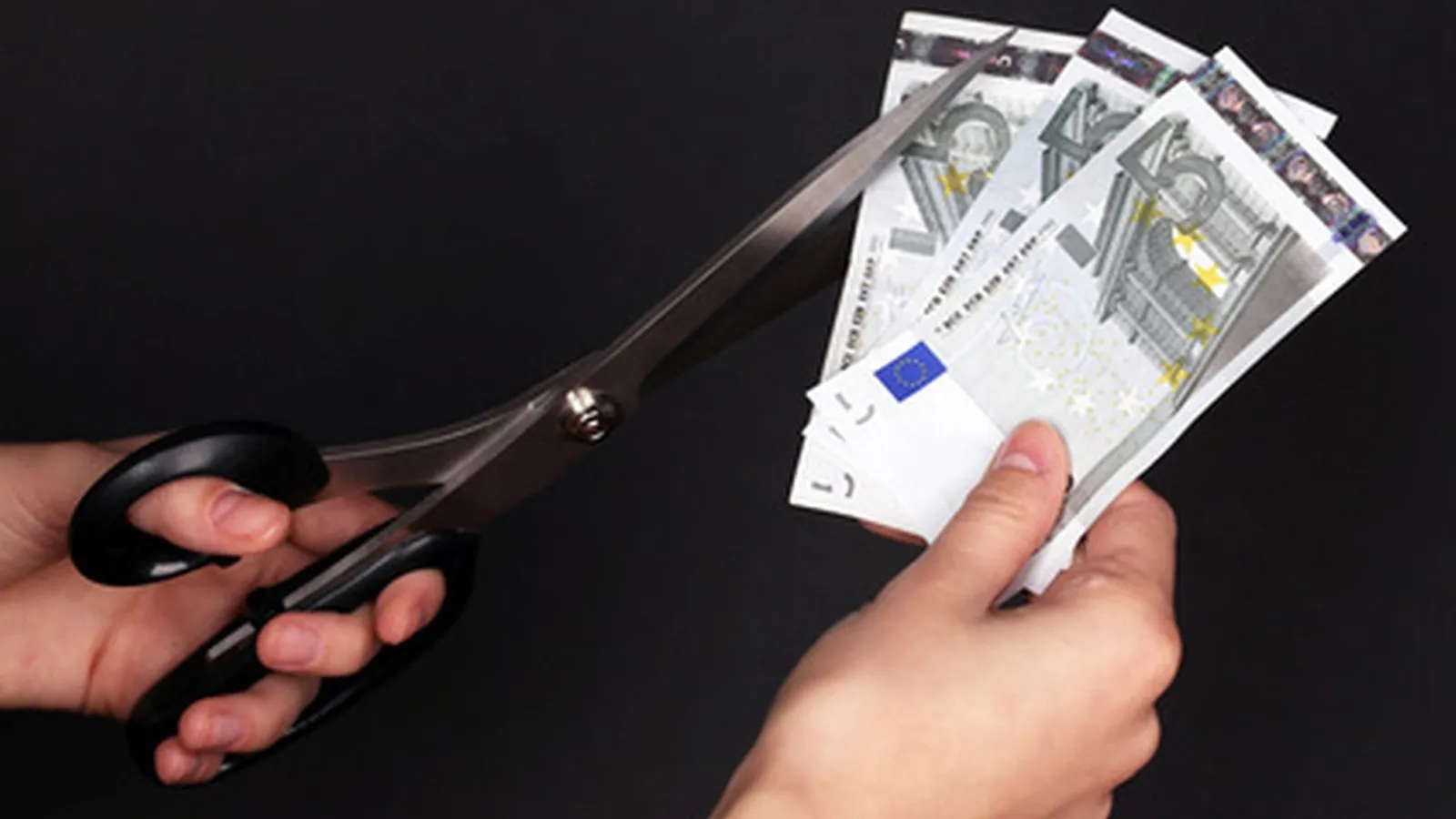 Jemand hält drei 5 Euro Scheine in der einen Hand und eine Schere daneben in der anderen Hand.