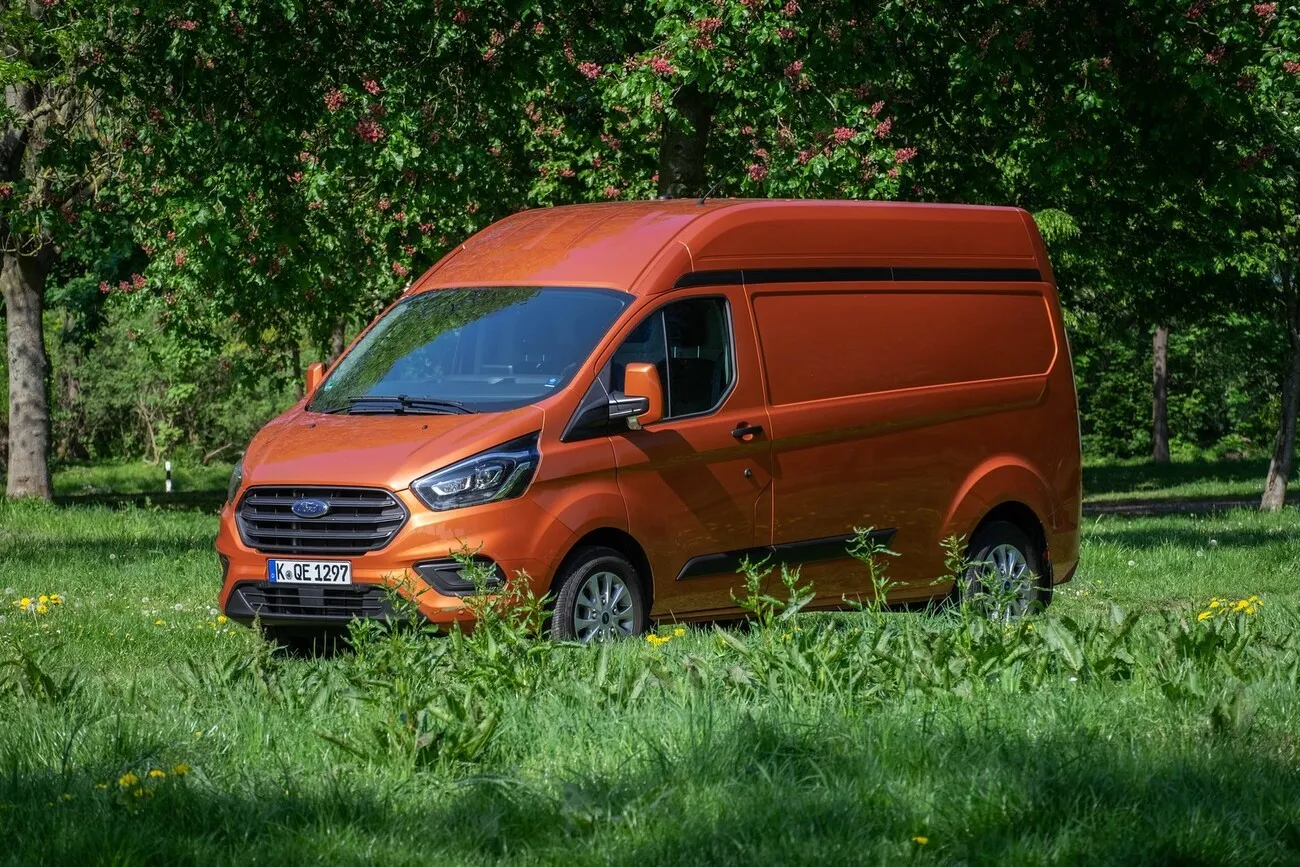 Der Ford Transit Custom in einer grünen Landschaft mit vielen Bäumen im Hintergrund.