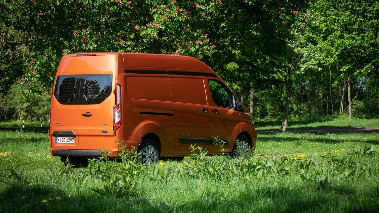 Der orangene Ford Transit Custom in seitlicher Ansicht in einer grünen Landschaft.