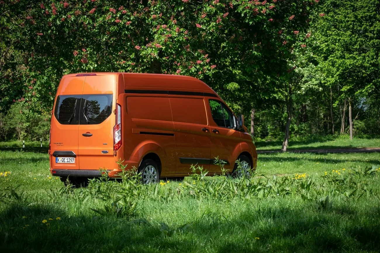 Der orangene Ford Transit Custom in seitlicher Ansicht in einer grünen Landschaft.