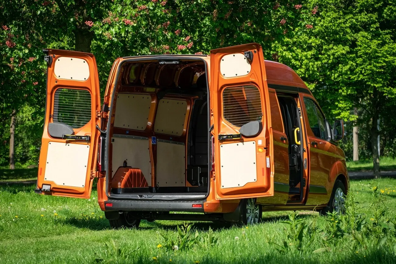 Der orangene Ford Transit Custom wird von hinten gezeigt mit geöffnetem Kofferraum und Blick ins Innere.