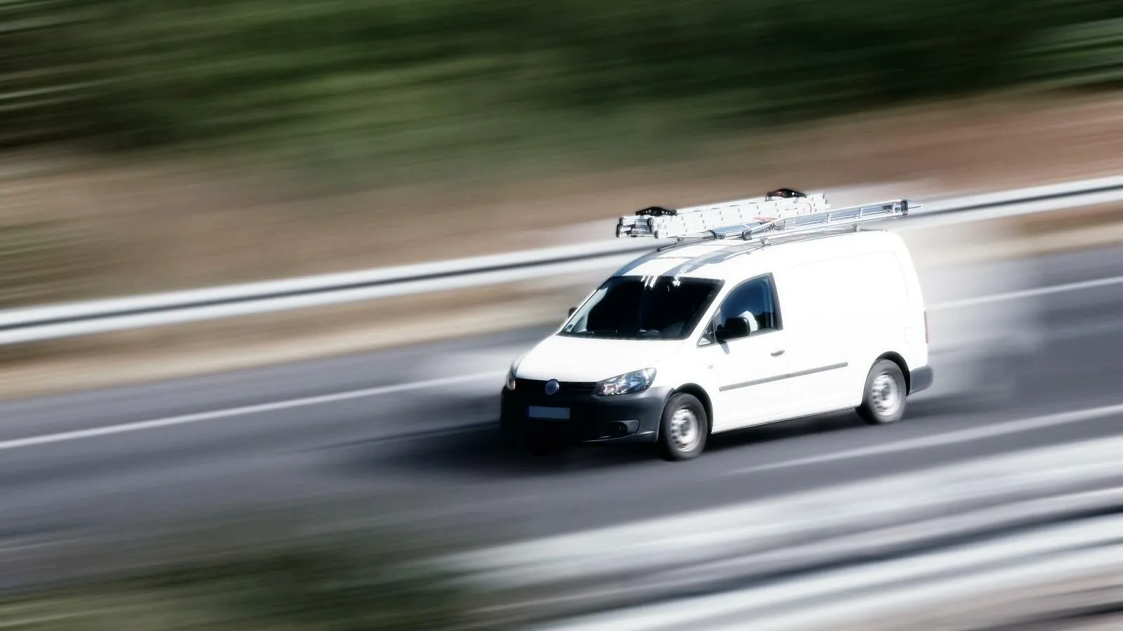 Ein weißer Transporter fährt auf einer Straße. Der Hintergrund ist verwischt.