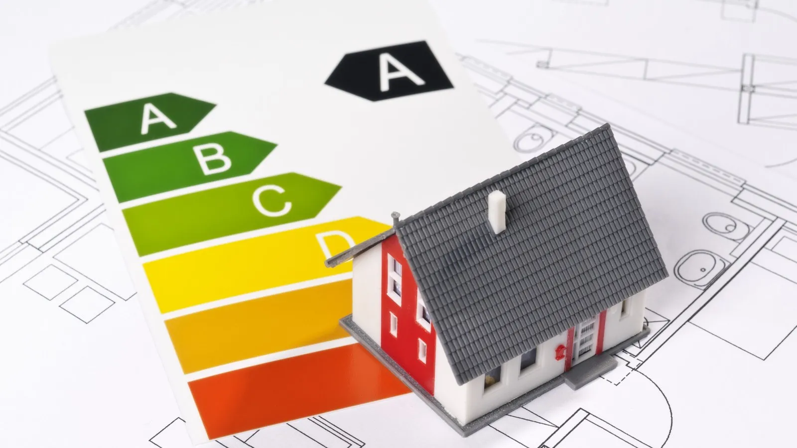 Ein Energielabel liegt auf einem Bauplan daneben steht ein kleines Haus.