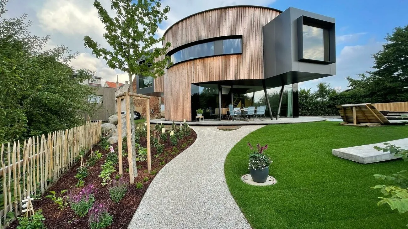 Das Drehhaus mit einer Holzoptik aus der Gartenansicht mit Blick auf den freischwebenden Teil des Drehhauses einen grauen Weg und grünen Garten.